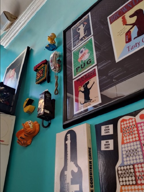 A colorful wall featuring vintage posters, a rotary phone, and quirky decor items like a Garfield figure and a game board.