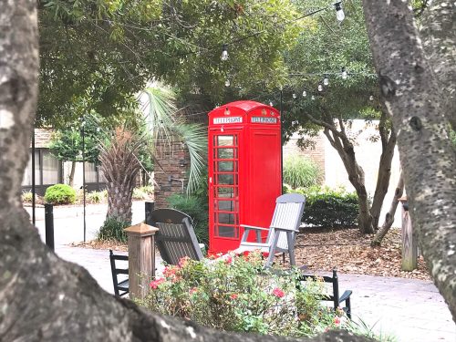 A red telephone booth surrounded by greenery and outdoor seating in a cozy garden setting.