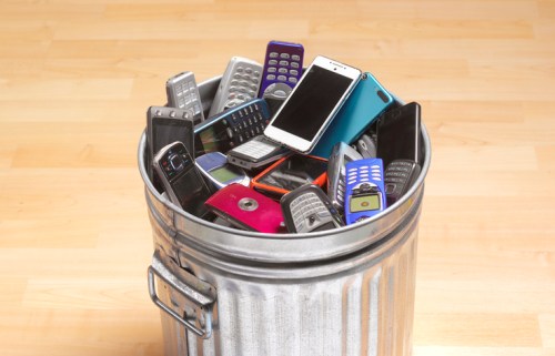 A metal trash can filled with various old mobile phones stacked inside.