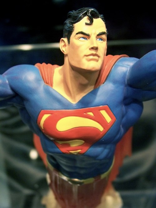 A close-up of a Superman statue, showcasing his iconic blue suit, red cape, and determined expression.