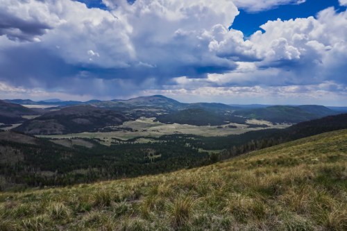 A panoramic view of rolling hills and valleys under a dramatic sky filled with clouds.