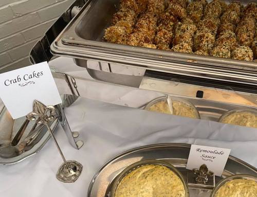 A serving tray with crab cakes and a bowl of remoulade sauce, accompanied by decorative labels.