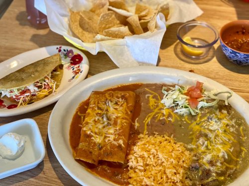 A plate of enchiladas with rice and beans, accompanied by a taco and a side of tortilla chips and salsa.