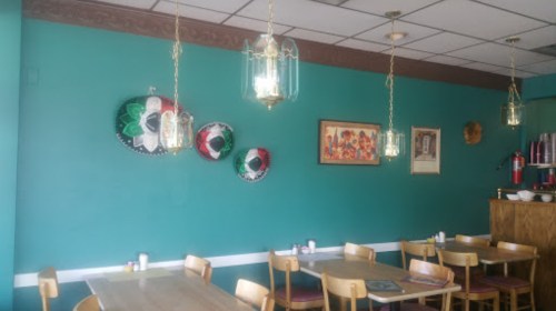 Colorful sombreros hang on a teal wall in a cozy restaurant with wooden tables and pendant lights.