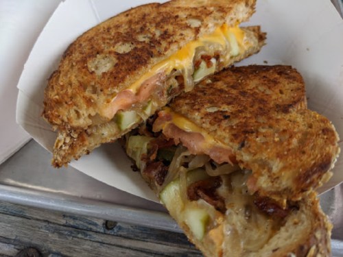 A toasted sandwich with melted cheese, pickles, and layers of meat, cut in half and served on a paper tray.
