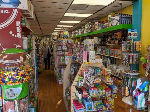 A colorful toy store aisle filled with various toys, games, and a gumball machine in the foreground.
