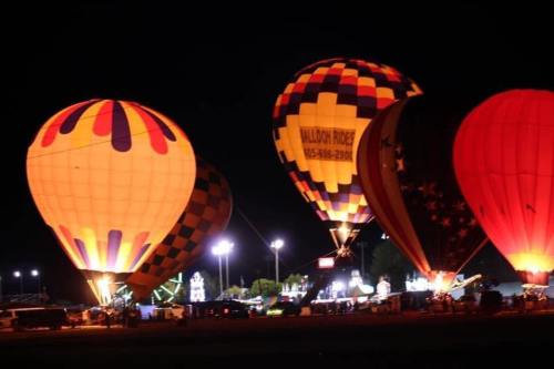 Colorful hot air balloons illuminated at night, with a festive atmosphere and lights in the background.