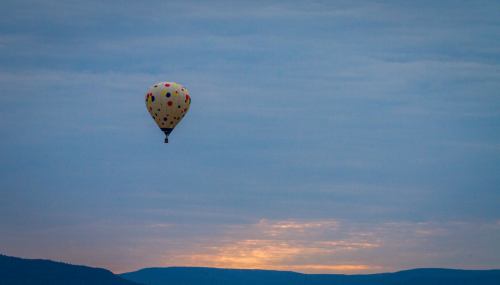 A colorful hot air balloon floats in the sky at sunset, with mountains in the background and a cloudy atmosphere.