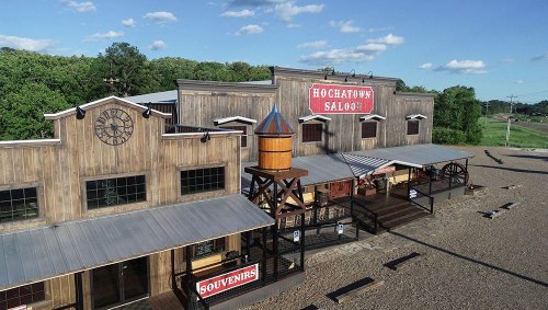 A rustic wooden building with a sign reading "Hochatown Saloon" and a water tower, set against a blue sky.