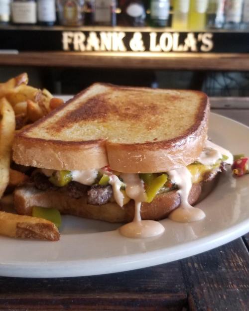 A grilled sandwich with beef, peppers, and sauce, served with a side of golden fries on a plate.