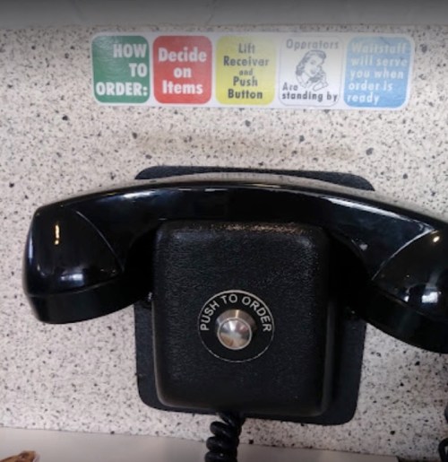 A black telephone on a counter with instructions for ordering displayed above it.