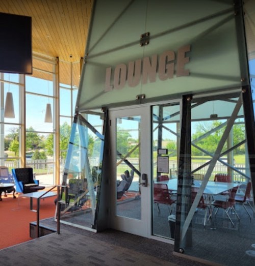 Modern lounge entrance with large glass doors, bright natural light, and a view of outdoor seating.