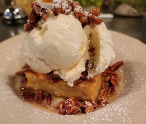 A warm dessert topped with vanilla ice cream and chopped pecans, dusted with powdered sugar on a plate.
