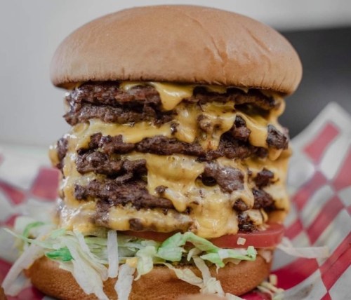 A towering burger with multiple beef patties, melted cheese, lettuce, and tomato, served in a toasted bun.