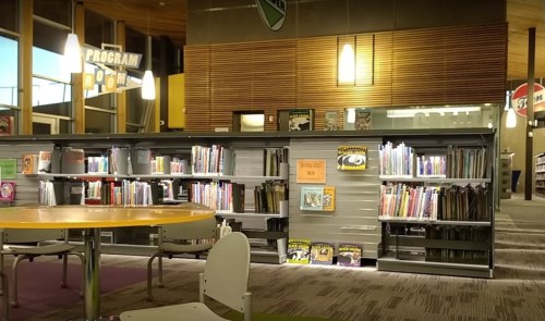 A cozy library interior featuring bookshelves, a round table, and colorful decor.
