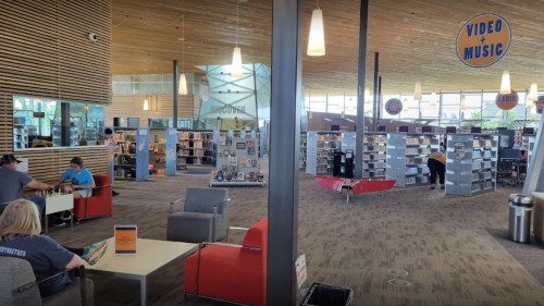 A spacious library interior with seating areas, shelves of books, and a section for video and music.