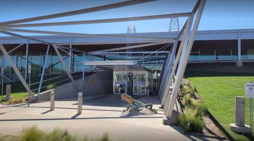 Modern building entrance with a unique architectural design and a large crab sculpture in front. Clear blue sky above.