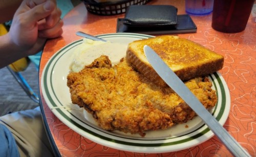 A plate with fried chicken, mashed potatoes, and toasted bread, set on a retro-style table.