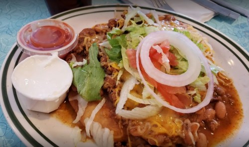A plate of enchiladas topped with lettuce, tomatoes, onions, cheese, and served with salsa and sour cream on the side.