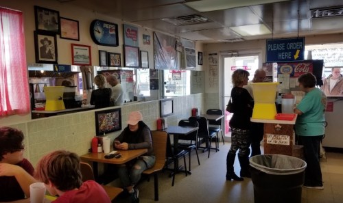 A busy diner interior with patrons at tables, a counter, and colorful decor on the walls.