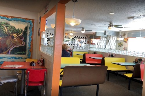 A colorful diner interior with red and yellow booths, a mural, and a view of the kitchen area in the background.