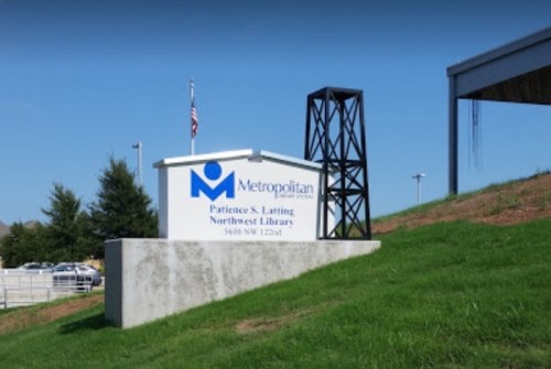 Sign for the Metropolitan Patience S. Latting Northwest Library, with green grass and a clear blue sky in the background.