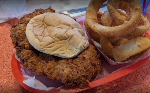 A fried chicken sandwich on a bun with a side of crispy onion rings in a red tray.