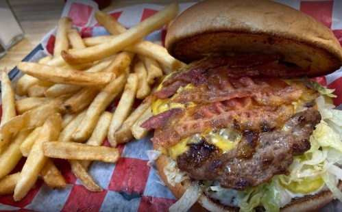 A juicy burger with bacon, cheese, and lettuce, served with a side of crispy French fries on a red and white checkered tray.