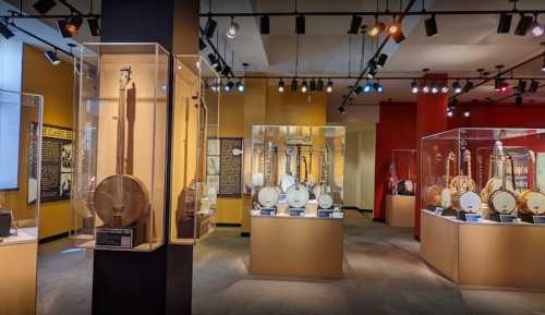 A museum exhibit featuring various banjos displayed in glass cases, with colorful walls and lighting.