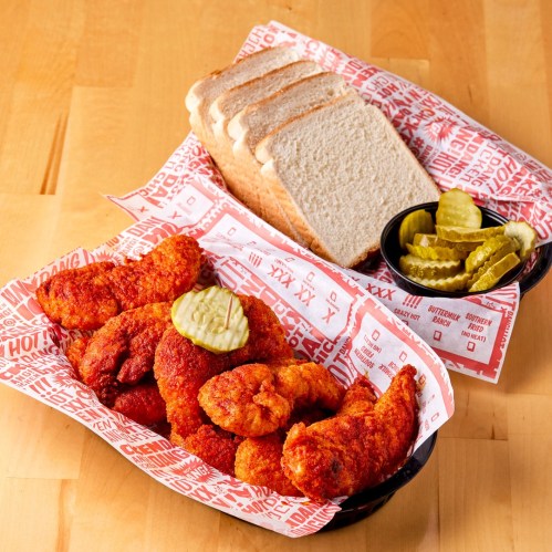 A platter of spicy fried chicken with pickles and slices of bread on a red patterned tray.