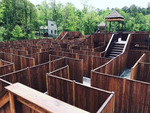 A wooden maze with high walls, surrounded by trees, featuring a gazebo in the center and a building in the background.