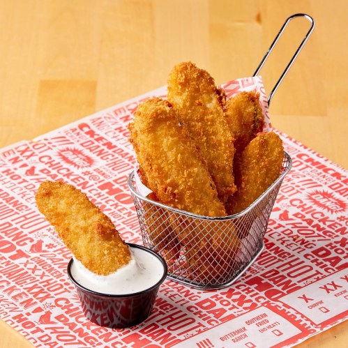 A basket of crispy chicken tenders with a side of dipping sauce on a patterned red paper.