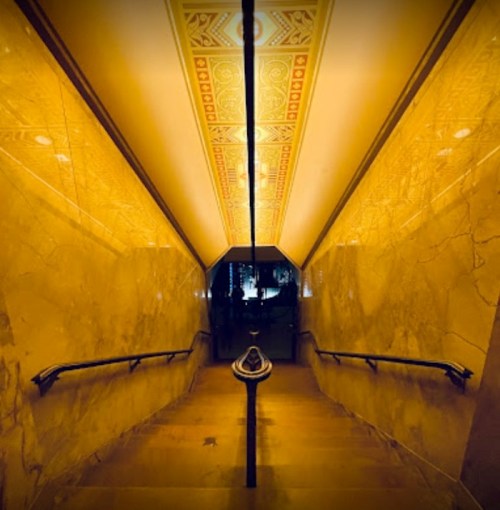 A dimly lit staircase with ornate golden walls and a decorative ceiling, leading downwards.