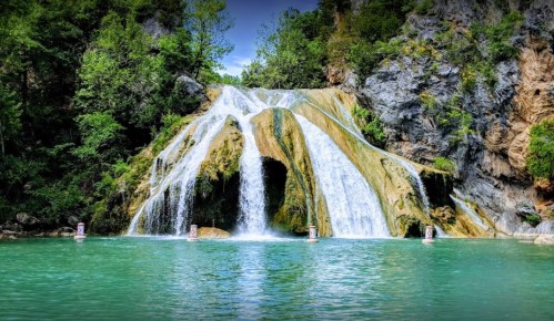 A serene waterfall cascading over rocky cliffs into a turquoise pool, surrounded by lush greenery.