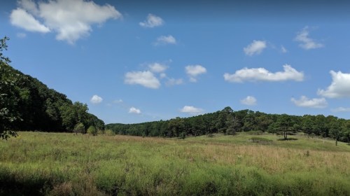 A scenic landscape featuring rolling hills, green fields, and a blue sky with fluffy white clouds.