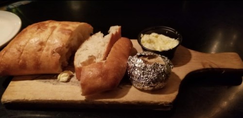 A wooden board with sliced bread, a small container of butter, and a foil-wrapped item.