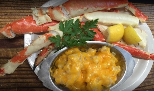A plate with crab legs, lemon wedges, and a side of cheesy macaroni. Garnished with parsley.