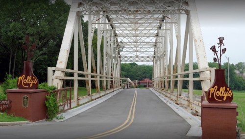 A white metal bridge with "Molly's" signage at both ends, leading to a green landscape and a building in the background.