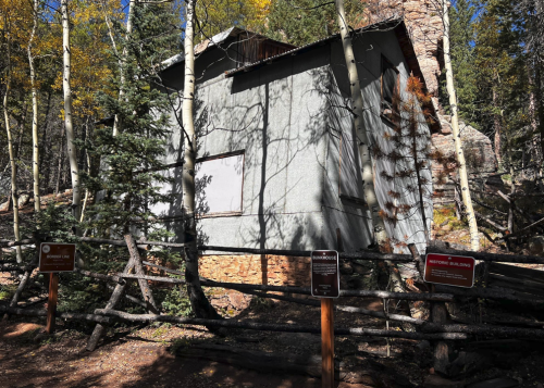 Abandoned building surrounded by trees and signs in a forested area, with autumn foliage visible.