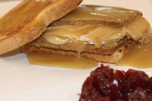 A sandwich with layers of turkey and gravy on toasted bread, served with a side of cranberry sauce.