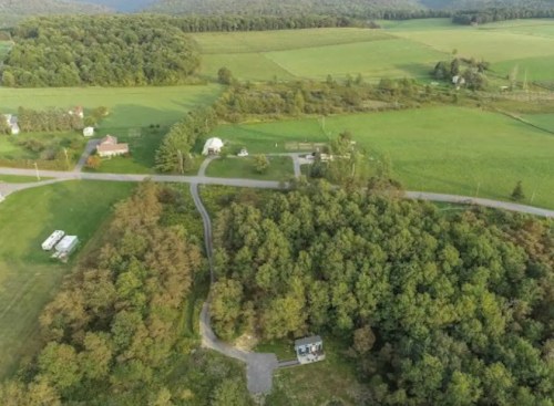 Aerial view of a rural landscape featuring green fields, scattered trees, and a winding road.