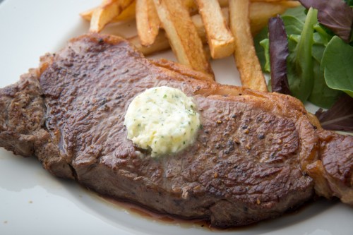 A juicy steak topped with herb butter, served with crispy fries and a side of mixed greens.