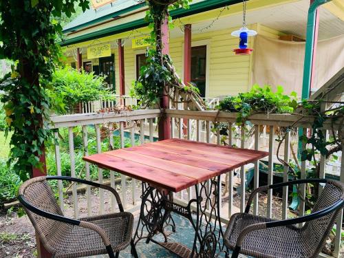 A cozy outdoor seating area with a wooden table and two chairs, surrounded by greenery and a colorful hummingbird feeder.
