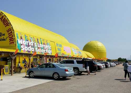 A bright yellow candy store with a large sign, featuring cars parked outside and people walking in.