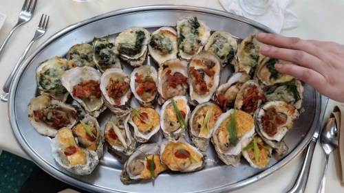 A large platter of assorted oysters topped with various ingredients, including spinach, bacon, and cheese.