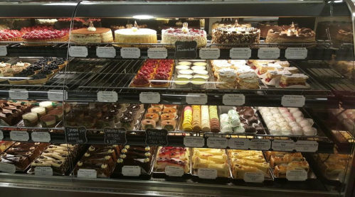 A display case filled with a variety of colorful cakes, pastries, and desserts, neatly arranged on shelves.