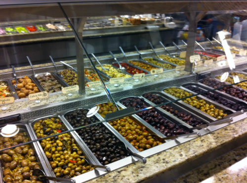 A variety of olives displayed in trays at a deli counter, with labels for different types.