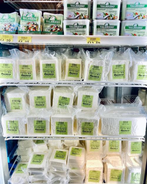 Shelves filled with packaged cheese blocks and containers, labeled with green tags, in a grocery store display.