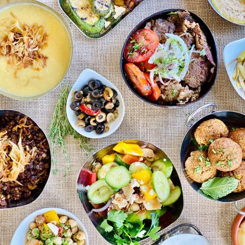 A colorful spread of various dishes, including salads, falafel, olives, and a creamy soup, arranged on a table.