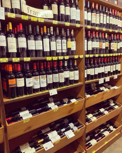 A wooden shelf filled with various bottles of wine, labeled with prices and country of origin.
